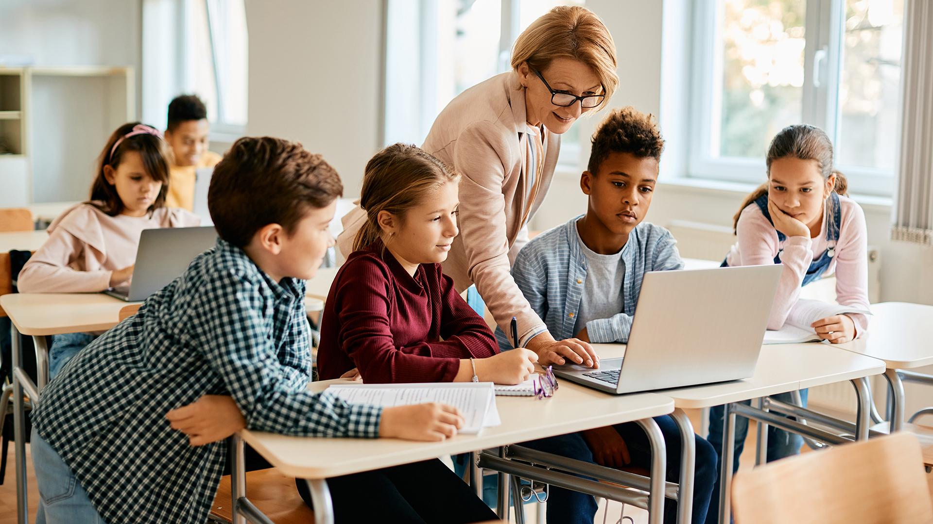 A teacher showing children something on her laptop in a classroom setting.