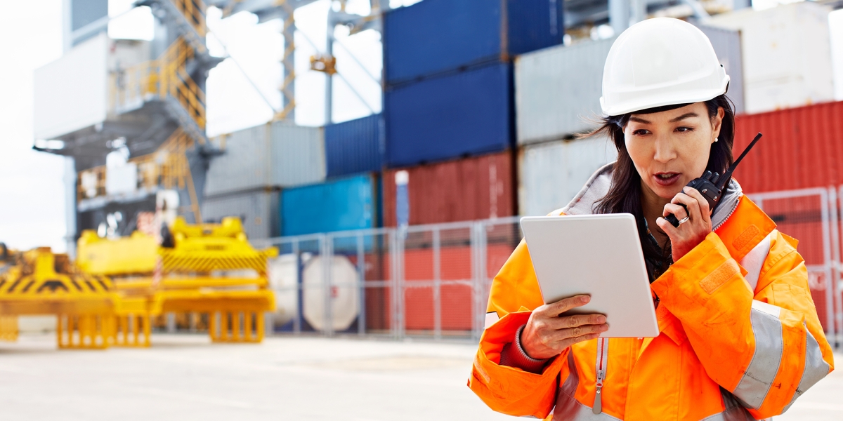 Female construction worker looking over important papers and speaking into walkie talkie.