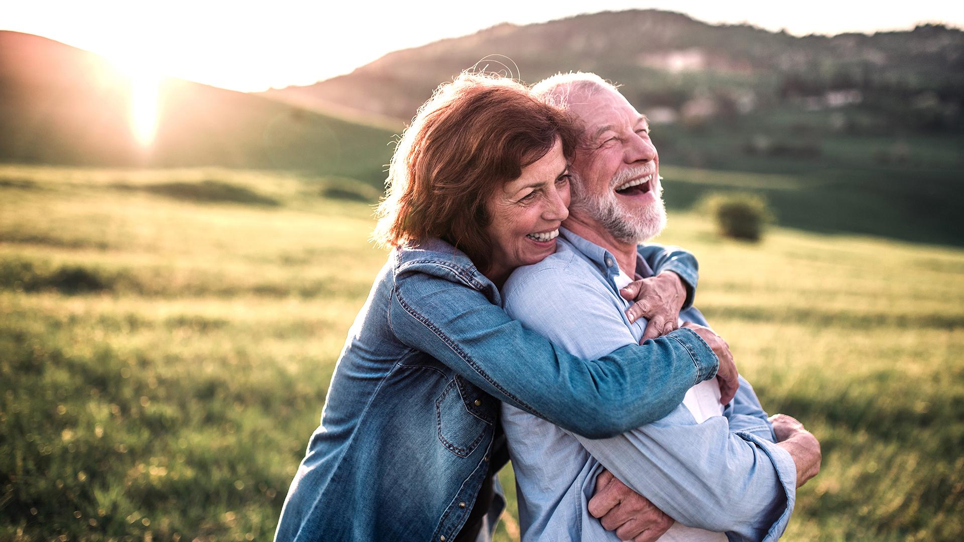 Side view of senior couple hugging outside in spring nature at sunset. 