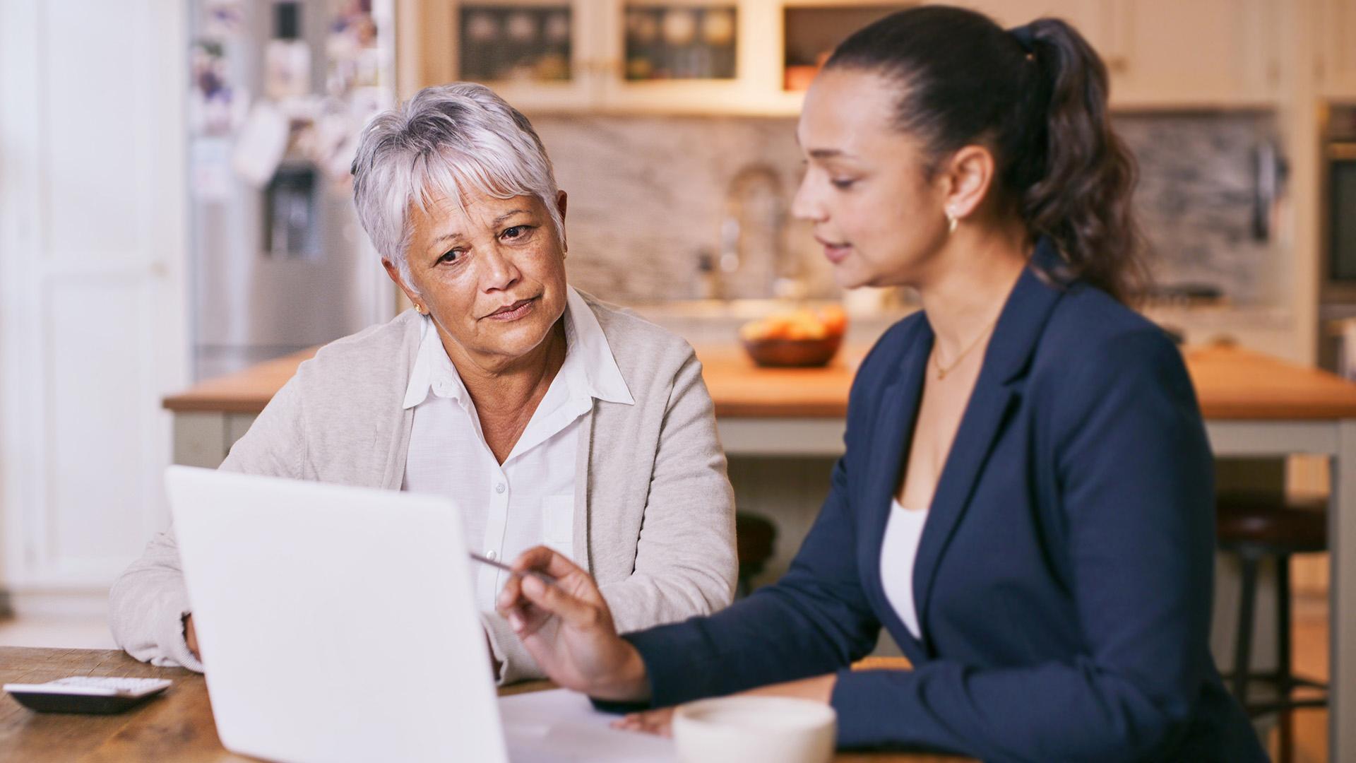 Two women at a desk going over contracts on a laptop.