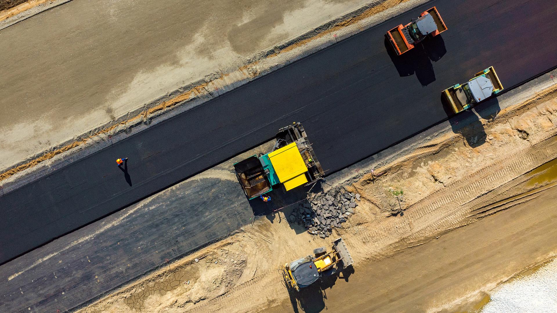 Four heavy machinery vehicles paving a cement road with one construction working nearby